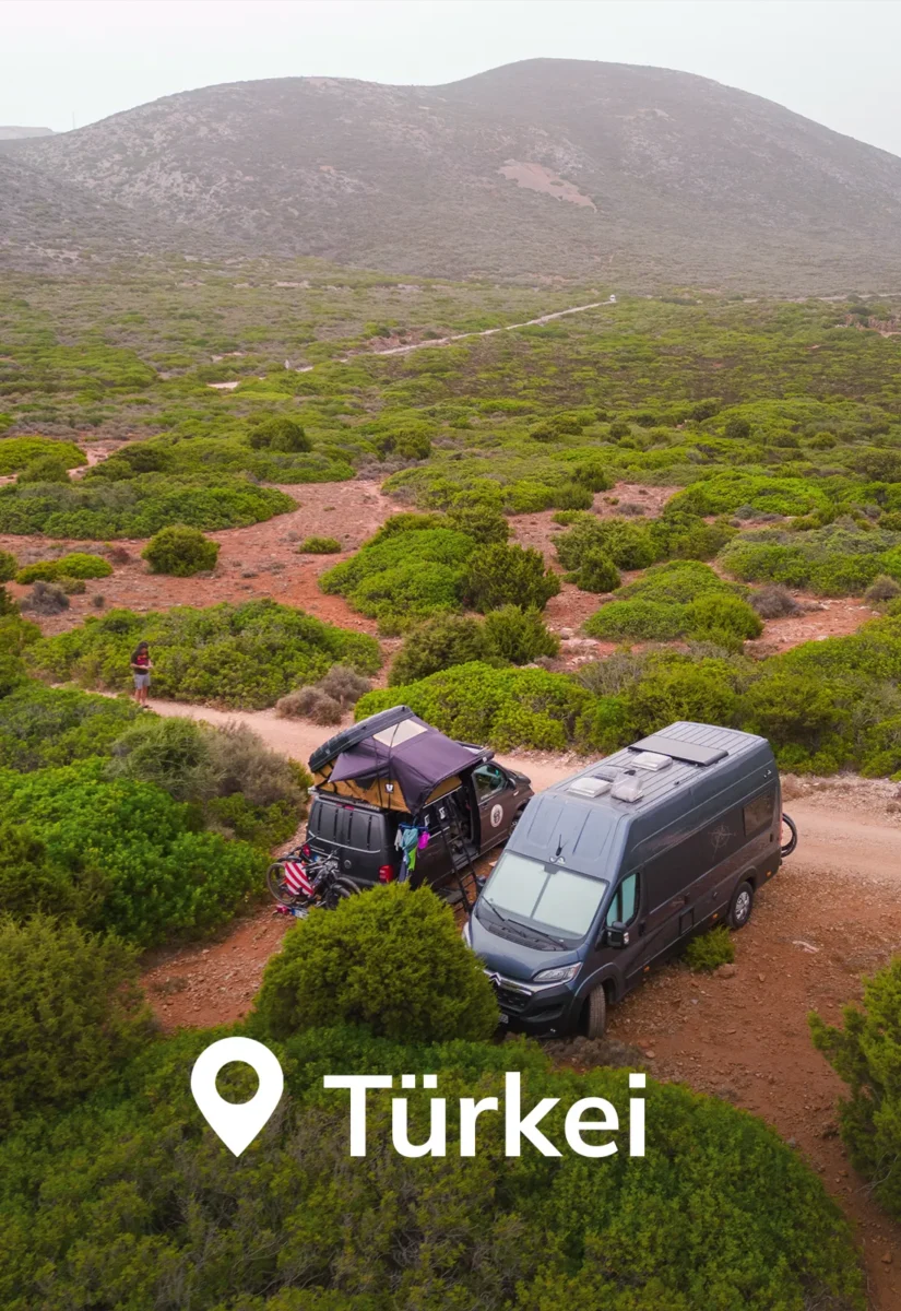 Zwei Camper stehen in einer grünen Landschaft mit Bergen im Hintergrund.