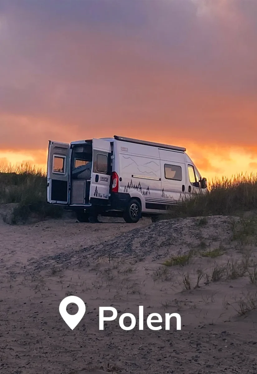 Weißer Camper steht bei Sonnenuntergang mit geöffneten Hecktüren auf einer Düne.