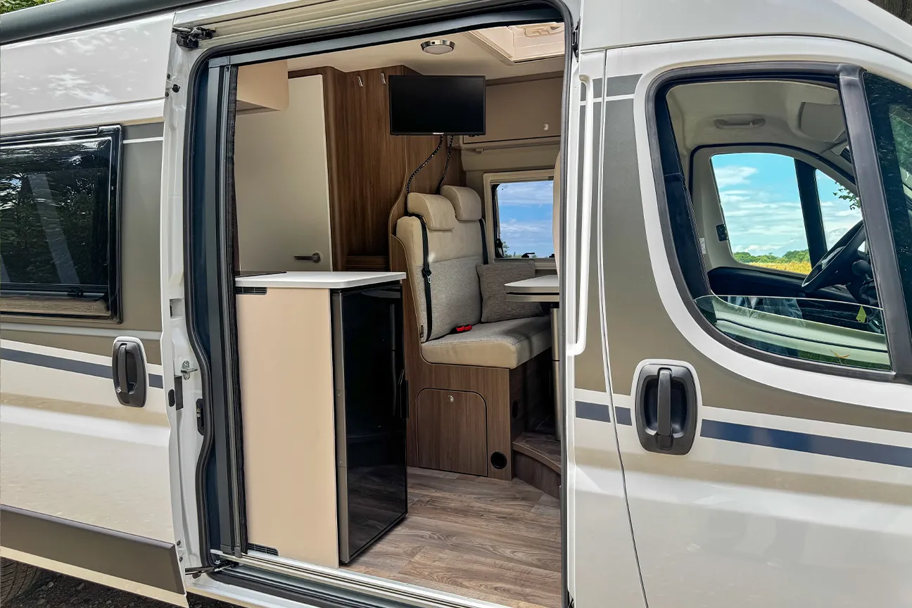 Sicht durch die geöffnete Seitentür eines weißen Fiat Carado Typ 640 Camper mit Blick auf eine einladende Sitzgruppe.