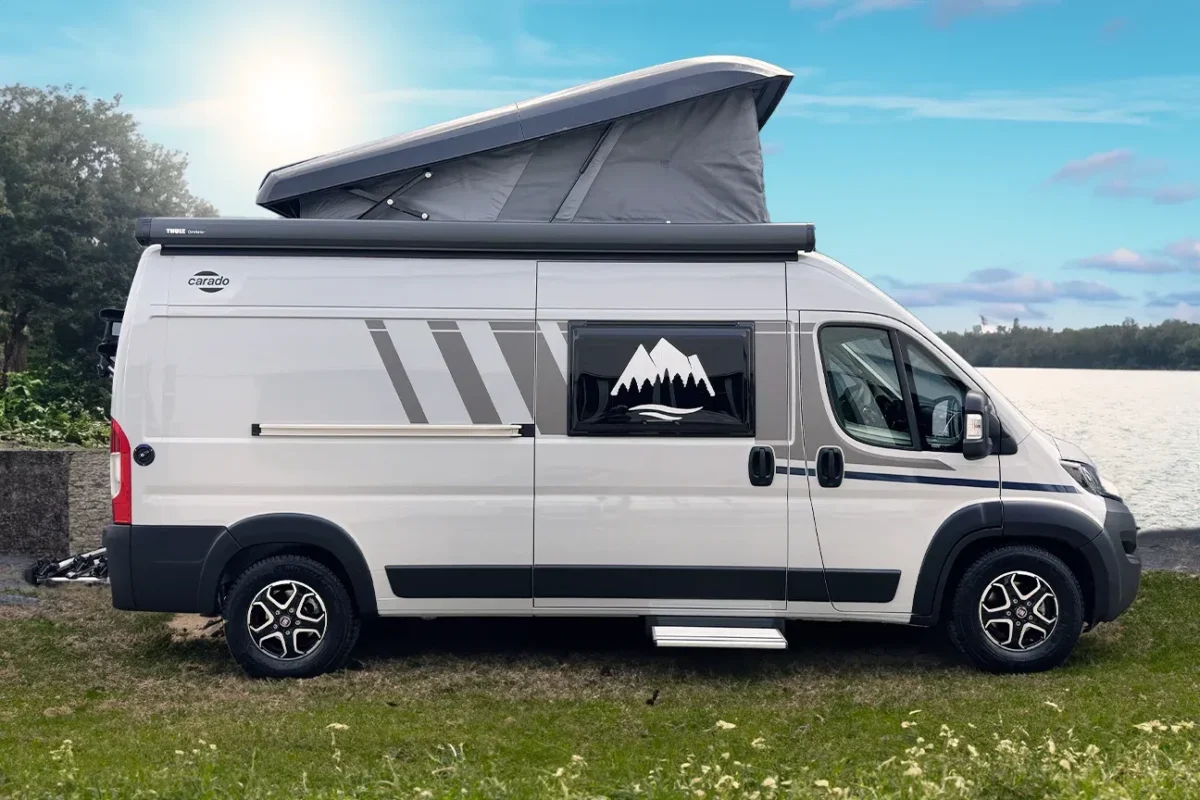 Seitlicher Blick auf einen weißen Camper, der auf einer grünen Wiese steht mit blauem Himmel im Hintergrund.