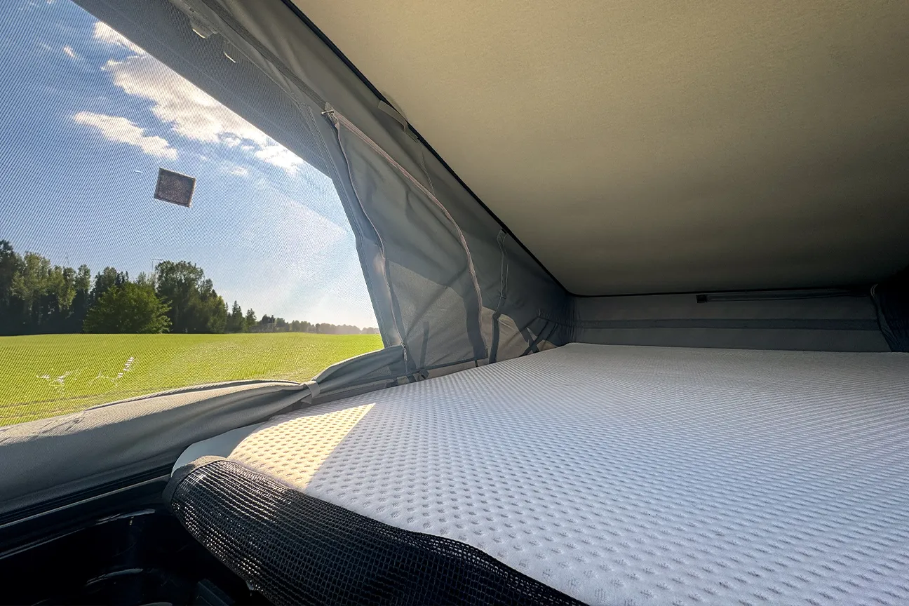 Liegefläche im Aufstelldach eines Fiat Carado Campervans mit Blick auf eine grüne Landschaft.