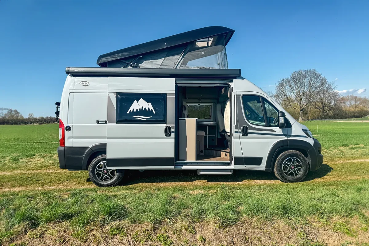 Seitlicher Blick auf einen weißen Fiat Carado Campervan mit Aufstelldach, der auf einem sonnigen Feld steht.