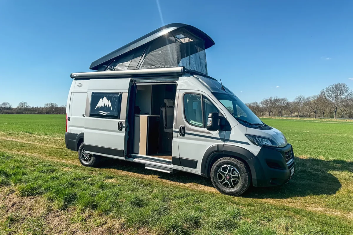 Schräger Blick auf den Fiat Carado Campervan mit Aufstelldach, der auf einem sonnigen Feld steht.