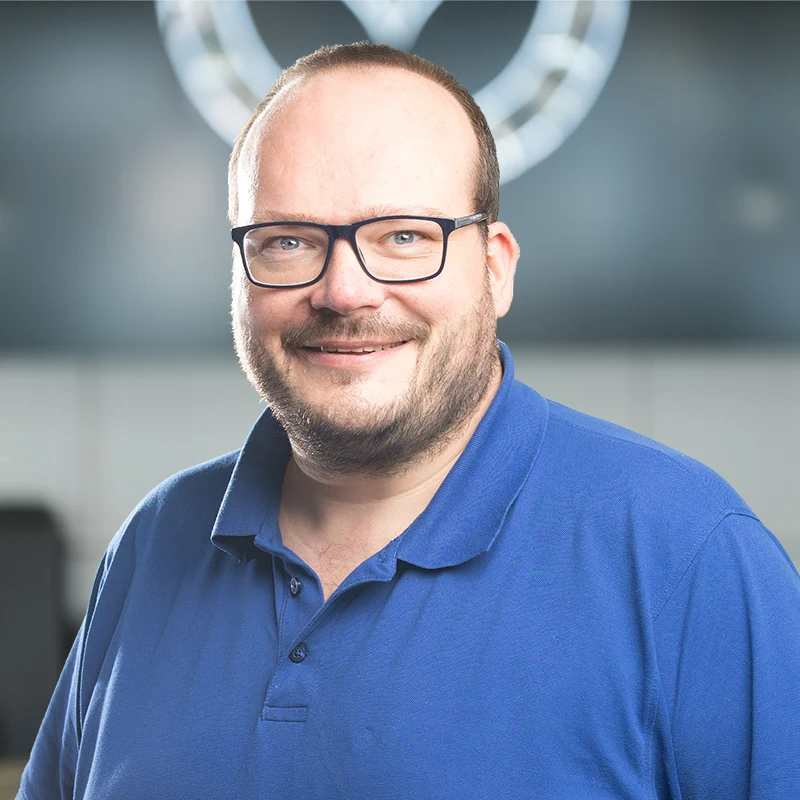 Mann mit blauem Poloshirt und Brille lächelt freundlich.